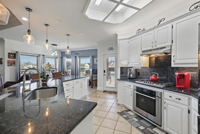 kitchen featuring under cabinet range hood, light tile patterned floors, decorative backsplash, stainless steel appliances, and a sink