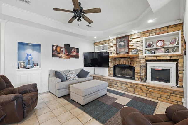 tiled living room with built in shelves, ceiling fan, a tray ceiling, ornamental molding, and a fireplace