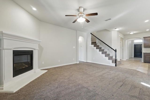 unfurnished living room with visible vents, stairway, light colored carpet, arched walkways, and a glass covered fireplace