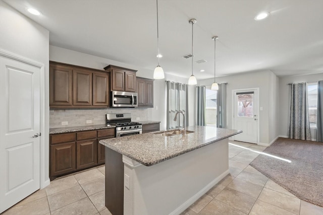 kitchen with an island with sink, a sink, appliances with stainless steel finishes, decorative backsplash, and light stone countertops