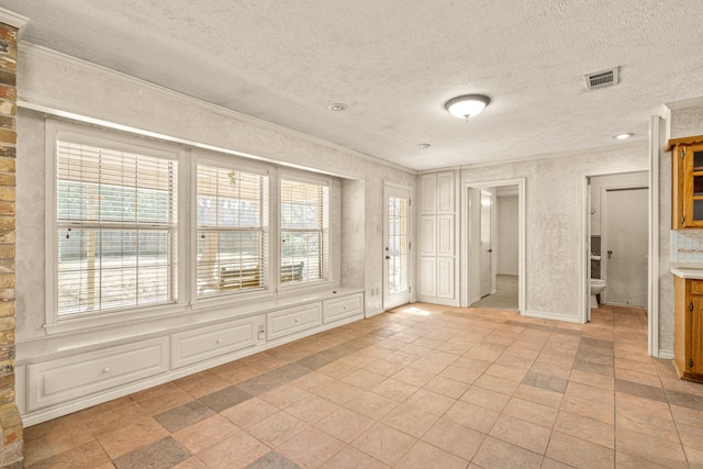 spare room with a wealth of natural light, visible vents, a textured ceiling, and crown molding