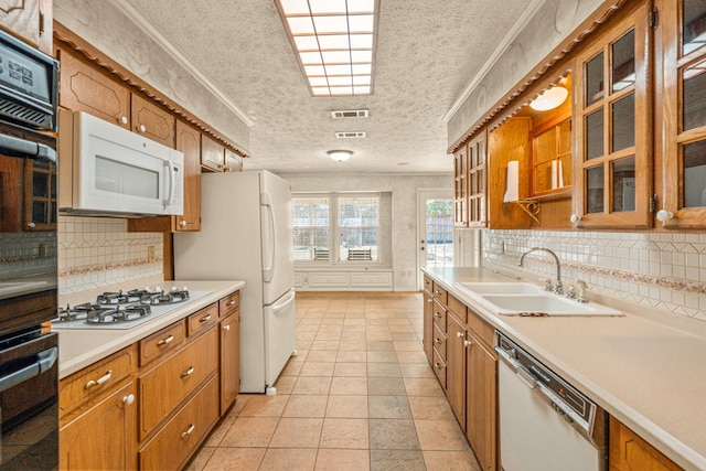 kitchen with visible vents, light countertops, brown cabinetry, white appliances, and a sink