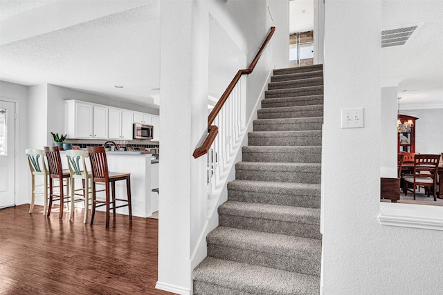 staircase featuring wood finished floors, baseboards, visible vents, a textured ceiling, and a textured wall