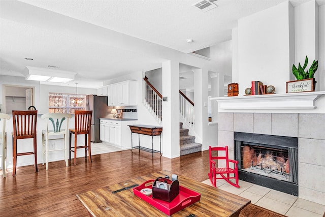 living area with a tiled fireplace, light wood-style flooring, stairs, and visible vents