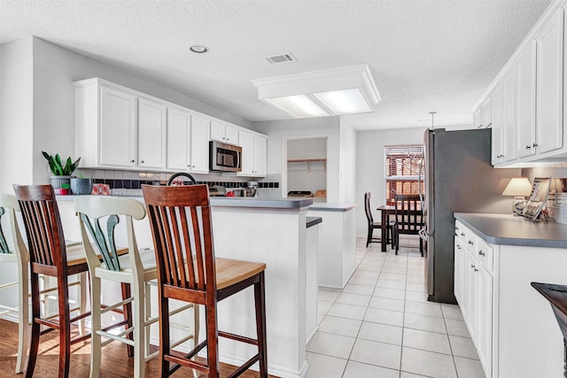 kitchen featuring visible vents, a peninsula, stainless steel appliances, decorative backsplash, and white cabinets