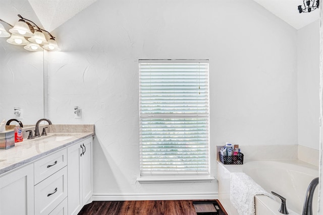 bathroom featuring vanity, wood finished floors, vaulted ceiling, a textured ceiling, and a bath