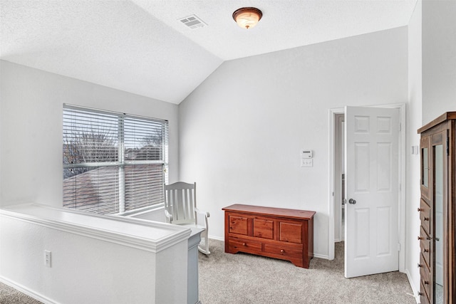 interior space featuring visible vents, lofted ceiling, a textured ceiling, and light carpet