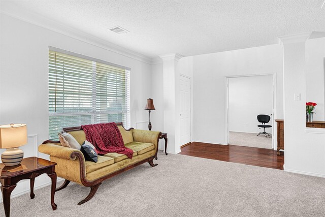 carpeted living area featuring visible vents, a textured ceiling, ornate columns, and ornamental molding