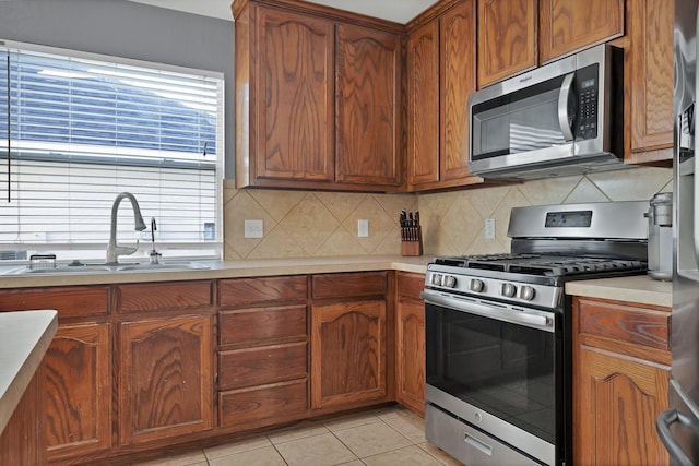 kitchen featuring light countertops, light tile patterned floors, decorative backsplash, appliances with stainless steel finishes, and a sink