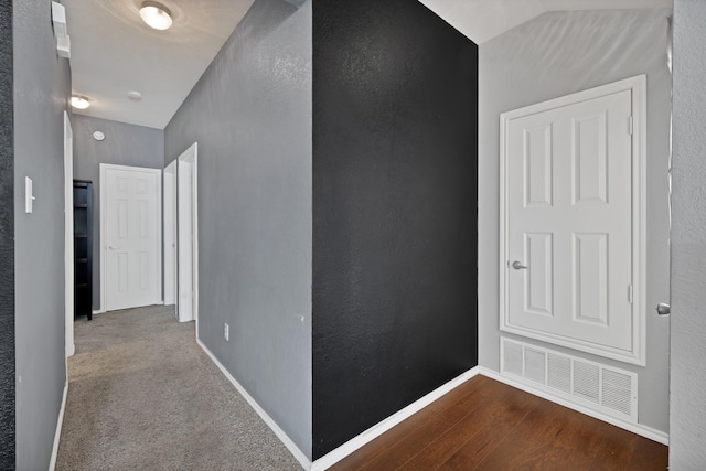 hall with visible vents, lofted ceiling, wood finished floors, baseboards, and a textured wall