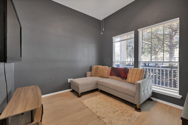 living area with a textured wall, baseboards, wood finished floors, and vaulted ceiling