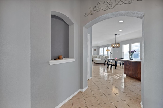 hall featuring light tile patterned floors, baseboards, and an inviting chandelier