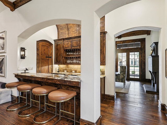 bar featuring decorative backsplash, baseboards, dark wood-style floors, and a towering ceiling