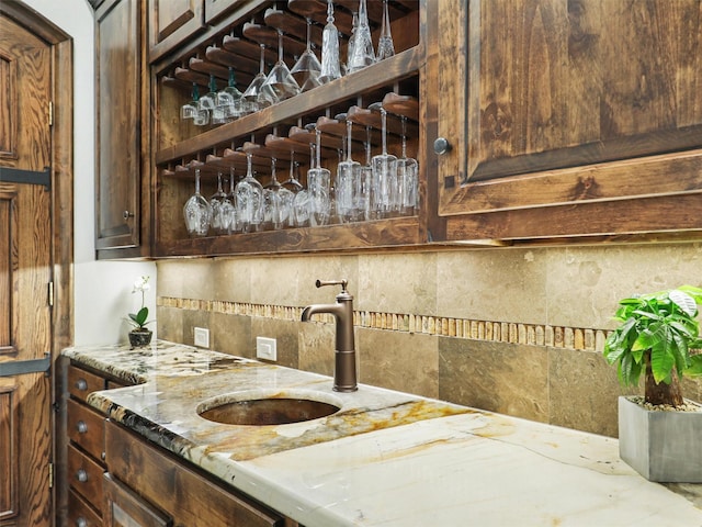 kitchen with a sink, light stone counters, backsplash, and dark brown cabinets