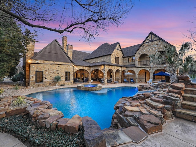 pool at dusk featuring a pool with connected hot tub and a patio area