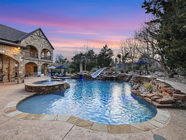 pool at dusk with a patio area and a pool with connected hot tub