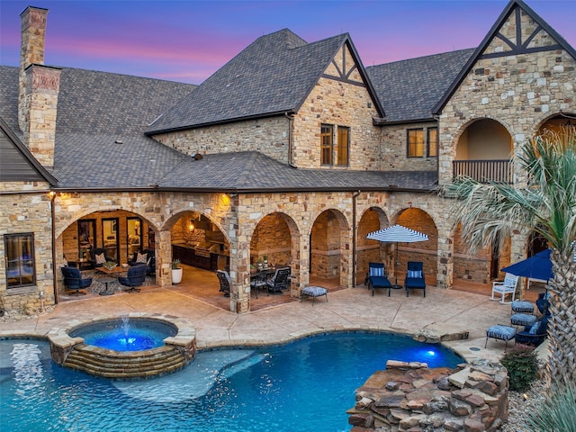 pool at dusk featuring a pool with connected hot tub and a patio