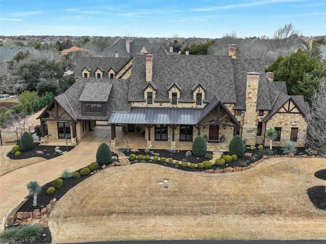 view of front of house with driveway, a standing seam roof, stone siding, metal roof, and a chimney