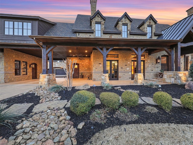 rear view of house featuring driveway, a standing seam roof, a porch, stone siding, and metal roof