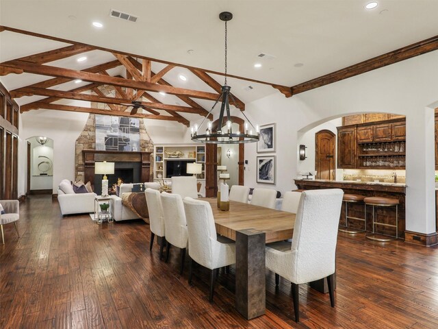 dining room with dark wood-style floors, visible vents, a fireplace, and beam ceiling