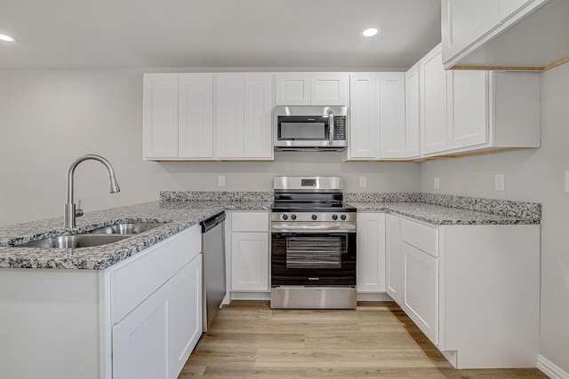 kitchen with light stone countertops, a peninsula, a sink, light wood-style floors, and appliances with stainless steel finishes