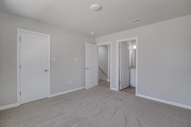 unfurnished bedroom featuring visible vents, carpet floors, a textured ceiling, and baseboards