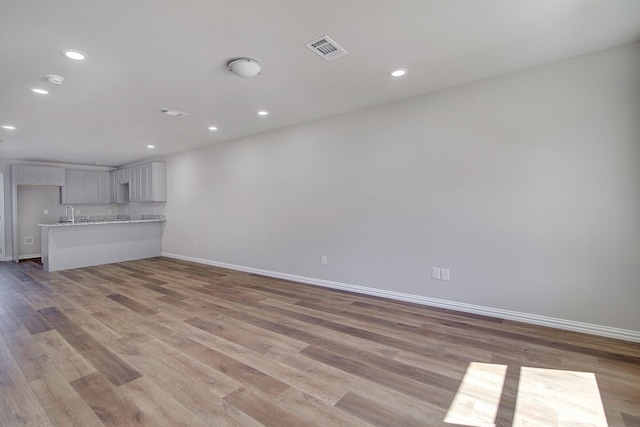 unfurnished living room with light wood-type flooring, visible vents, baseboards, and recessed lighting