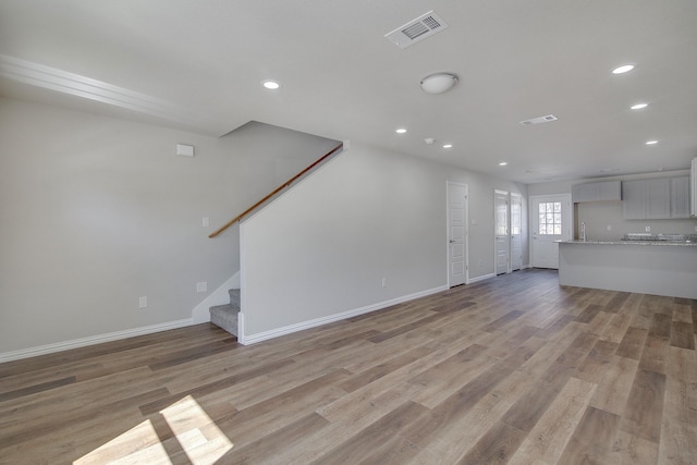 unfurnished living room with stairway, baseboards, visible vents, recessed lighting, and light wood-type flooring