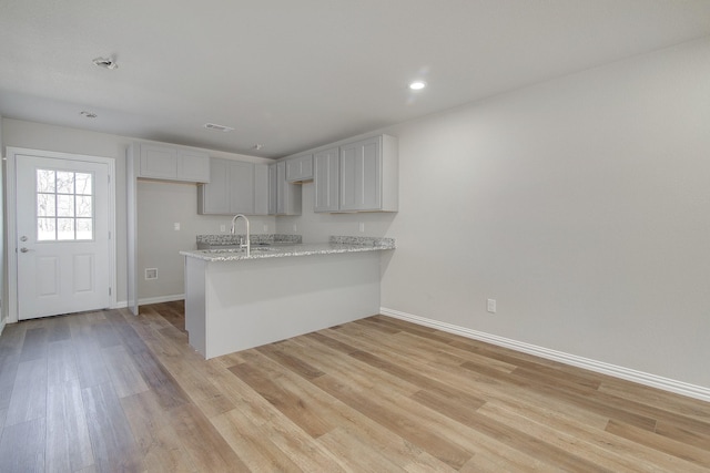 kitchen featuring a peninsula, light wood-style floors, baseboards, and light stone countertops