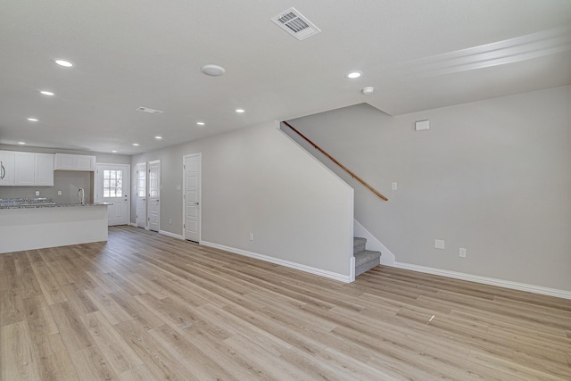 unfurnished living room with stairway, light wood-style floors, visible vents, and a sink