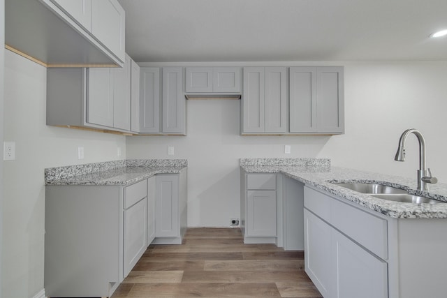 kitchen with gray cabinets, light stone countertops, light wood-style floors, and a sink