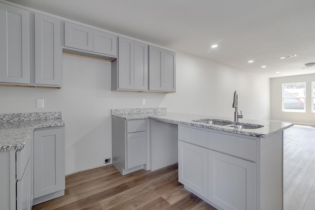 kitchen featuring gray cabinetry, light stone countertops, light wood-type flooring, and a sink