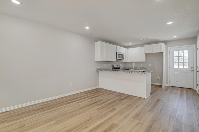 kitchen with light stone countertops, a peninsula, light wood-style flooring, stainless steel appliances, and white cabinets