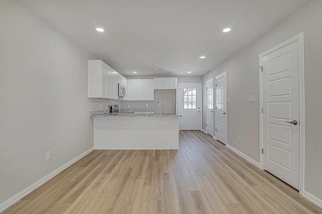 kitchen with stainless steel microwave, baseboards, light wood-type flooring, a peninsula, and white cabinetry