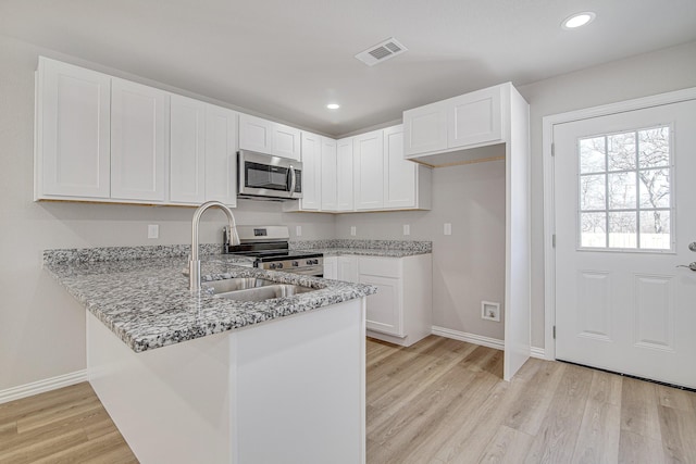 kitchen featuring light stone counters, visible vents, a peninsula, a sink, and stainless steel appliances