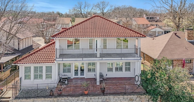 rear view of property featuring fence private yard, french doors, a tile roof, and a balcony