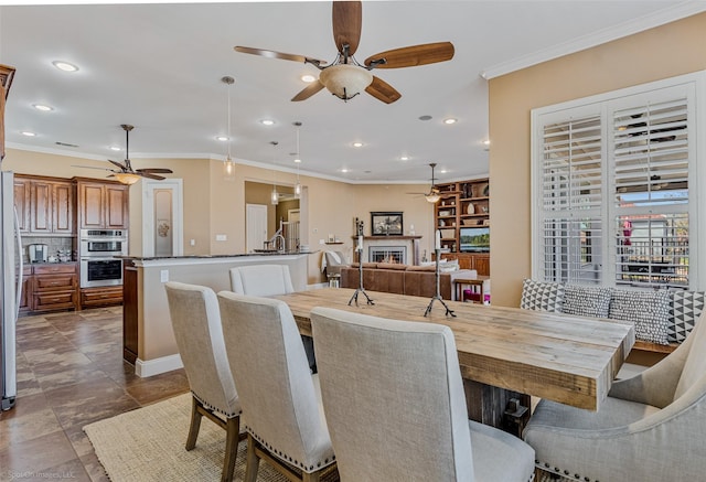 dining area featuring recessed lighting, crown molding, a lit fireplace, and ceiling fan