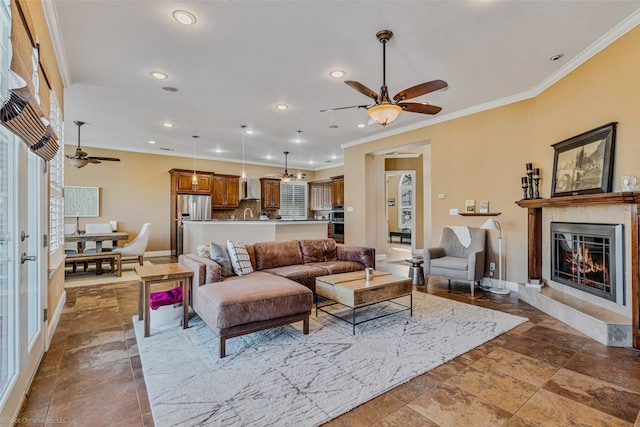 living area with a glass covered fireplace, recessed lighting, crown molding, baseboards, and ceiling fan