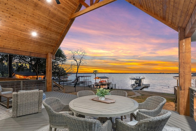 deck at dusk with outdoor dining space, a water view, and a boat dock