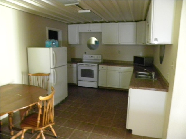 kitchen with a sink, white appliances, dark tile patterned flooring, and white cabinets