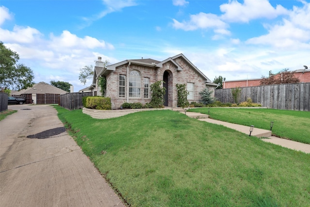 view of front facade with brick siding, a chimney, a front yard, and fence