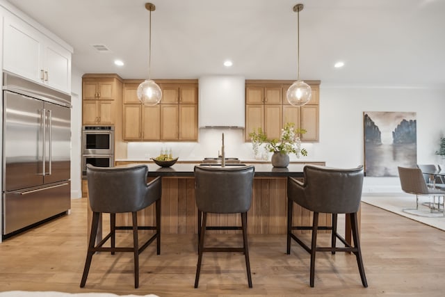 kitchen with visible vents, premium range hood, stainless steel appliances, hanging light fixtures, and light wood-type flooring