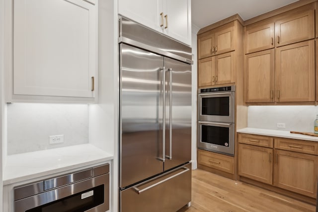 kitchen with light stone counters, light wood-type flooring, and built in appliances