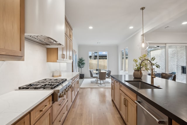 kitchen featuring light wood finished floors, premium range hood, decorative light fixtures, stainless steel appliances, and a sink