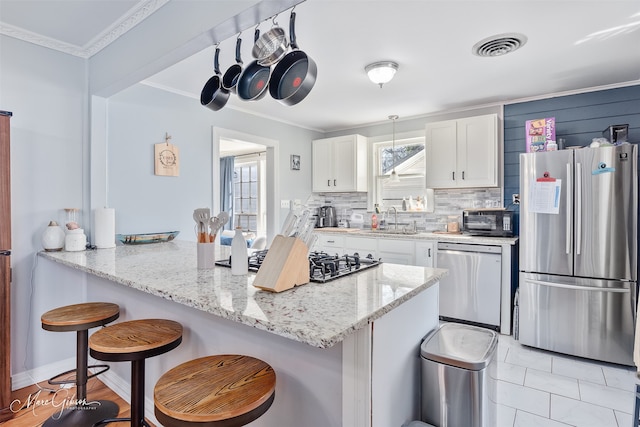 kitchen with a kitchen bar, stainless steel appliances, a peninsula, white cabinets, and crown molding