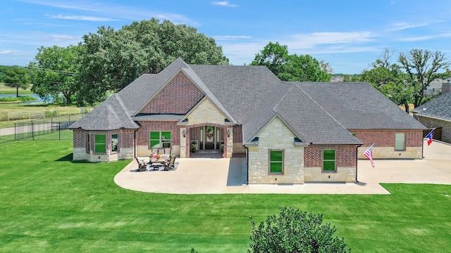 rear view of property with fence, roof with shingles, a yard, stone siding, and a patio