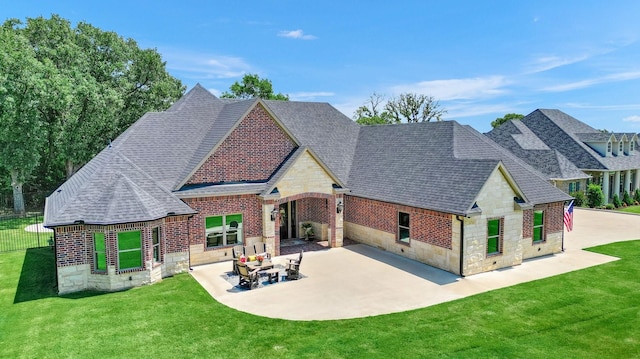 rear view of house featuring a shingled roof, a patio area, stone siding, a lawn, and brick siding