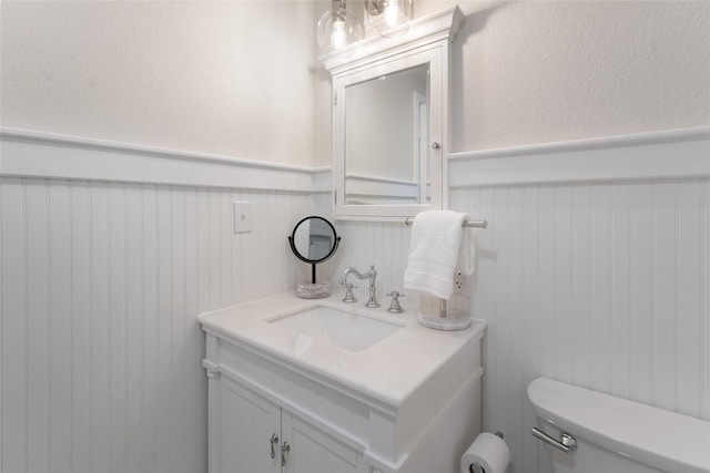 half bathroom with wainscoting, toilet, and vanity