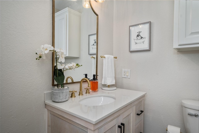 half bathroom featuring toilet, vanity, and a textured wall