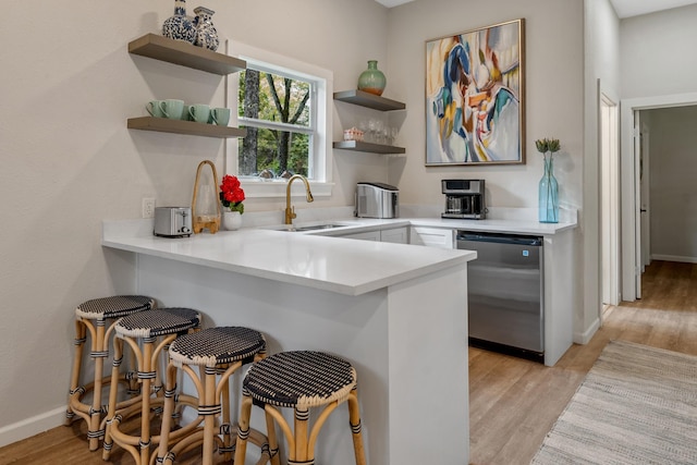 kitchen with a sink, light wood-style flooring, a kitchen breakfast bar, a peninsula, and open shelves